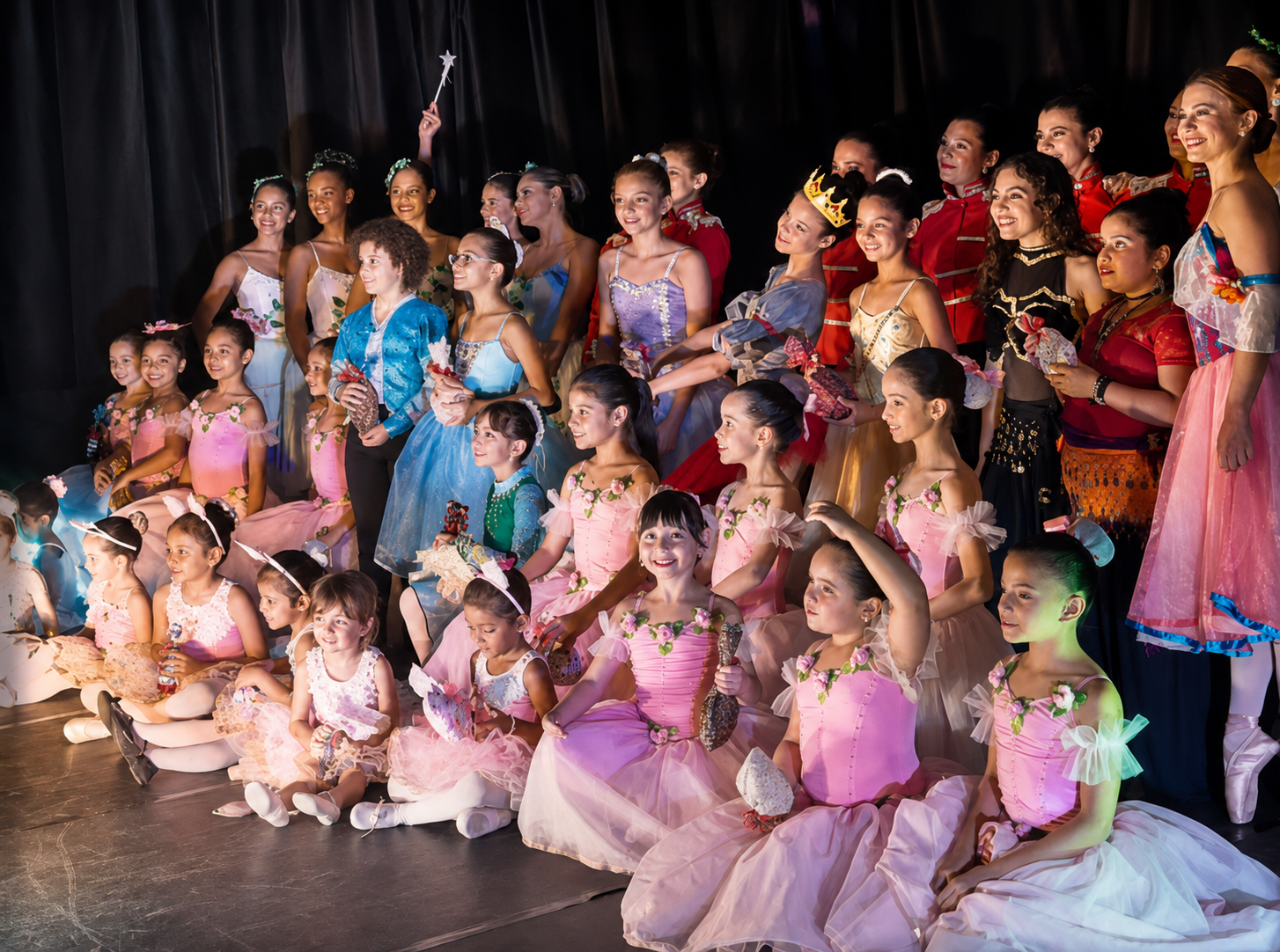 Grupo de crianças e jovens em figurinos de dança reunidos no palco após apresentação.